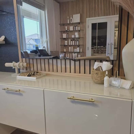 White dresser with gold handles in a room with a large mirror and decorative elements.