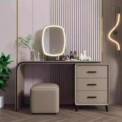 A modern vanity desk set in a styled room, featuring a three-drawer cabinet, a square ottoman, a built-in oval mirror with a glowing LED light frame, and decorative items on top.
