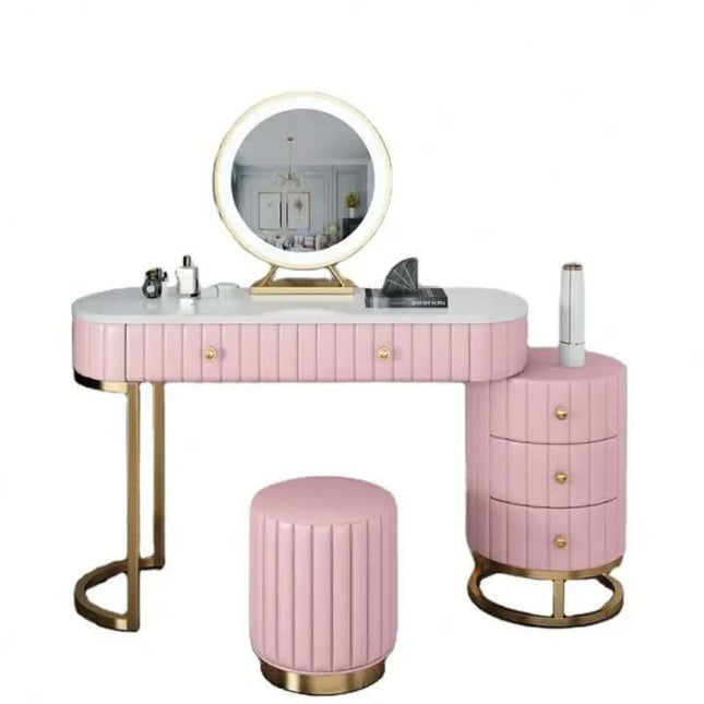 Pink vanity table set with a round illuminated mirror, three drawers on the right, a matching round stool, and gold-tone legs and drawer pulls, shown on a white background.