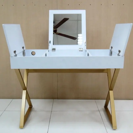 A white vanity desk with a rectangular mirror on top, flanked by two hinged side panels, and supported by gold-tone metal legs, shown against a wood-paneled wall.
