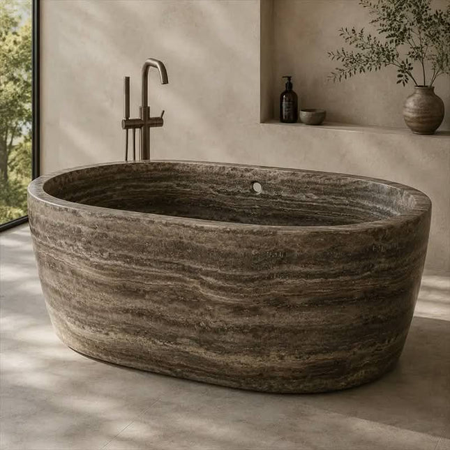 A freestanding oval bathtub made of natural stone with dark gray and brown marbled striations, shown in a minimalist bathroom setting with a matte bronze faucet and a recessed shelf in the background.