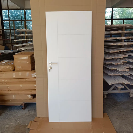 White door with a gold handle in an industrial setting with stacks of materials.