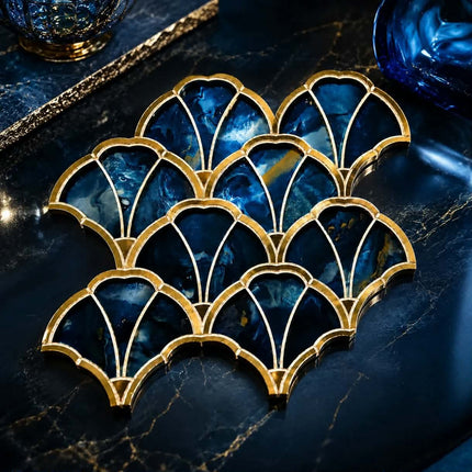 A set of nine scalloped coasters with gold metal frames and deep blue marbled stone inserts, arranged on a dark marble surface.