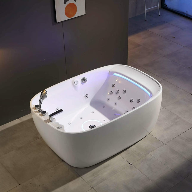 A white freestanding bathtub with multiple jet nozzles and built-in lighting, shown in a modern bathroom setting with gray tiled floors and a dark wall.