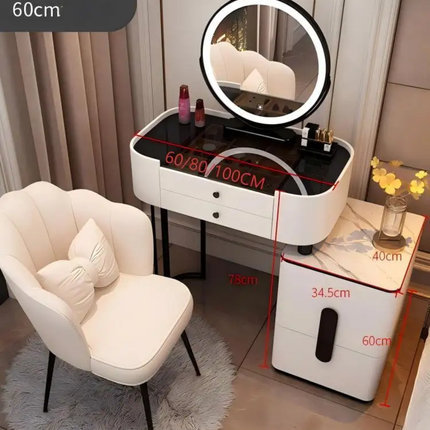 A white vanity table set with an illuminated round mirror, black top surface, two drawers, and a matching side cabinet, shown in a styled room with a white upholstered chair. Red dimension lines and text overlay indicate measurements such as 60/80/100CM, 75CM, 34.