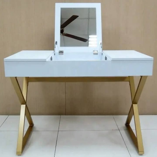 A white vanity desk with a built-in mirror and gold metal legs, set against a light wood-paneled wall and tiled floor.