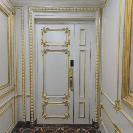 Decorative white door with gold molding in a room with ornate wall trim.