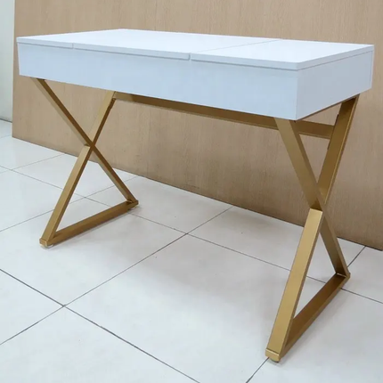 A modern vanity desk with a white rectangular top and a gold-finished X-shaped metal frame, shown on a tiled floor against a light wood-paneled wall.