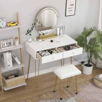 A white vanity table with gold metal hairpin legs, a round backlit mirror, two open drawers, and a matching white stool, styled in a bright room with a plant, shelf, and decor.