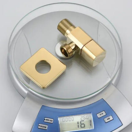 Gold-colored plumbing valve and square washer on a digital scale