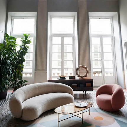 Modern living room with a curved beige sofa, pink chair, and round coffee table.