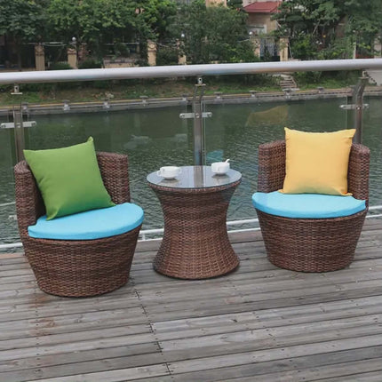Outdoor furniture set with wicker chairs and table on a wooden deck by a body of water.