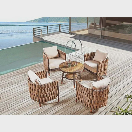 Outdoor patio set with wicker chairs and table on a wooden deck by a pool and ocean view.