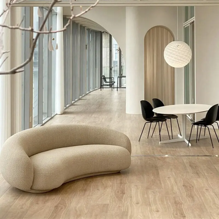 Modern interior with a curved beige sofa, round white table, and black chairs.