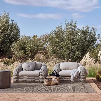 Two wicker chairs on a patio with a scenic background of trees and sky.