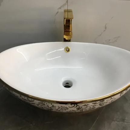 White oval sink with gold decorative rim and faucet on a gray countertop.