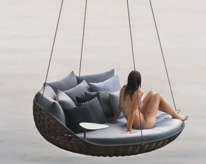 Person sitting on a hanging outdoor chair with cushions against a neutral background