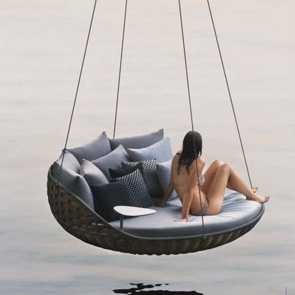 Person sitting on a hanging outdoor chair with cushions against a neutral background
