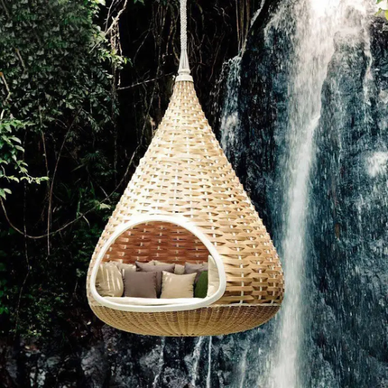 Woven hanging chair with cushions in front of a waterfall