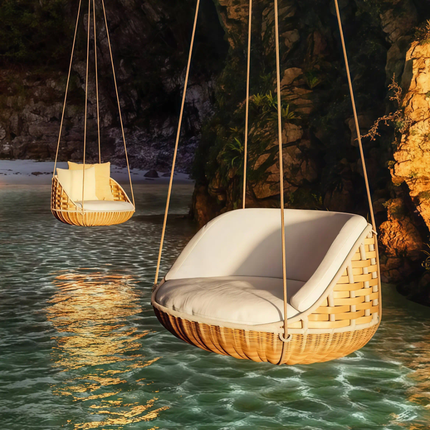 Wicker swings with white cushions hanging over water at sunset.
