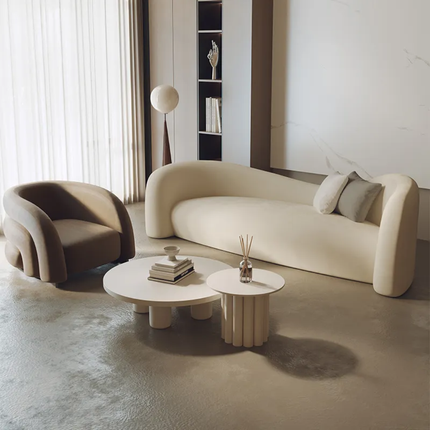 Modern living room with beige sofa and armchair, round coffee table, and decorative items.