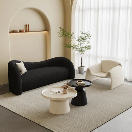 Modern living room with a black sofa, white armchair, and round coffee tables.