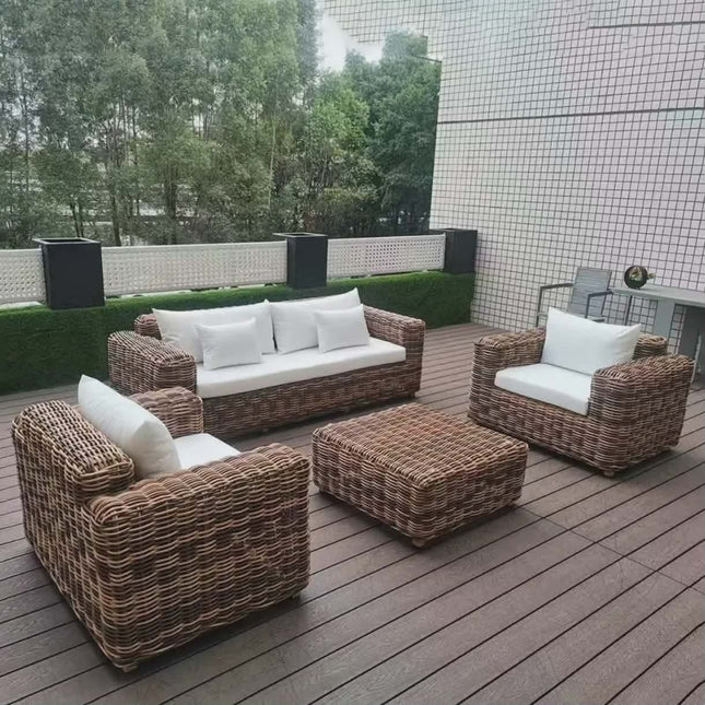 Wicker outdoor furniture set on a wooden deck with a tiled wall and greenery in the background.