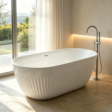A freestanding oval bathtub with a ribbed exterior and a polished chrome faucet, shown in a modern bathroom with large windows, beige walls, and tiled flooring.