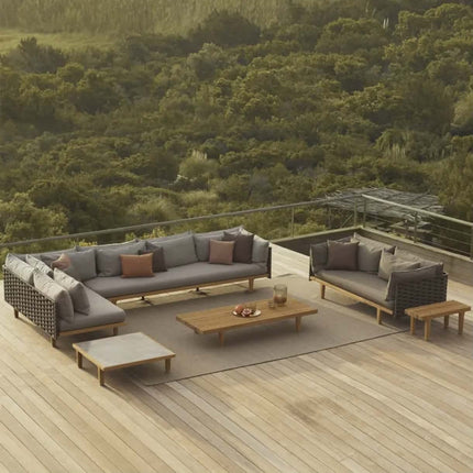 Outdoor patio furniture set with cushions on a wooden deck overlooking a forest.