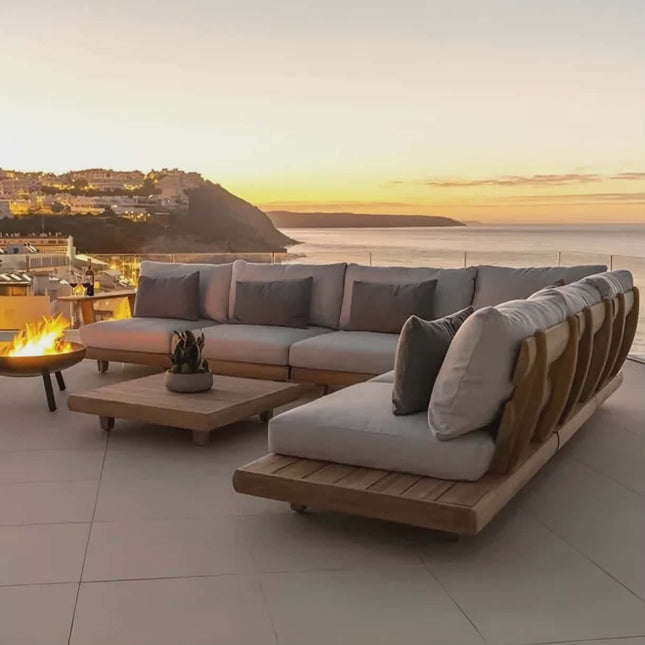 Outdoor patio set with sectional sofa and fire pit table on a deck overlooking a scenic sunset.