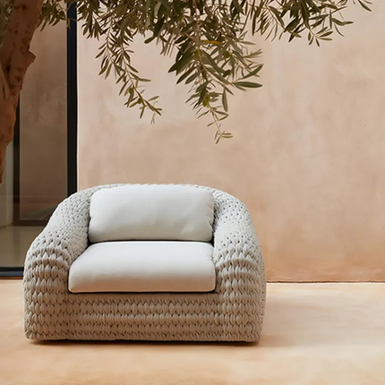 Beige armchair with white cushion against a beige wall with greenery