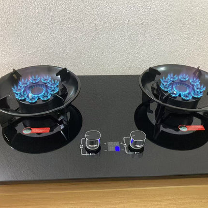 Two gas burners on a black stove with blue flames against a white wall.