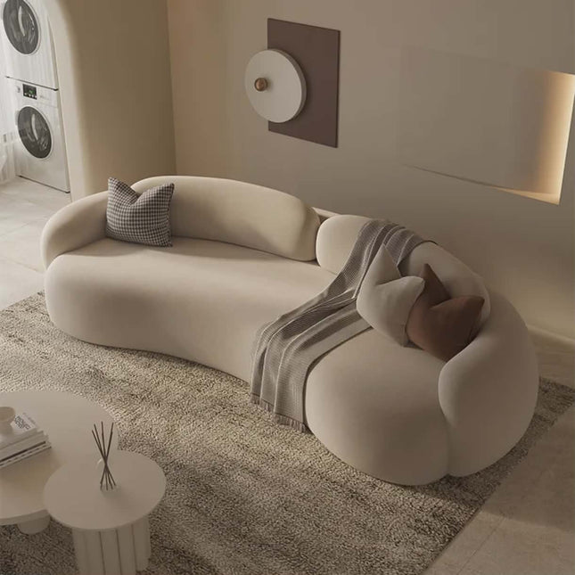 Modern beige sofa with decorative pillows and a blanket in a living room setting.