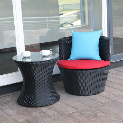 Black wicker chair with red cushion and blue pillow on a wooden deck.