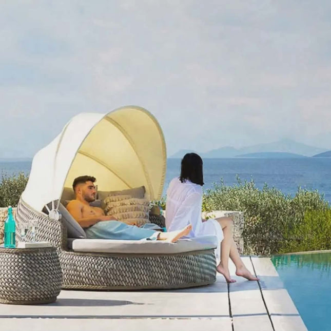 Two people relaxing on a sunbed by a pool with a scenic view.