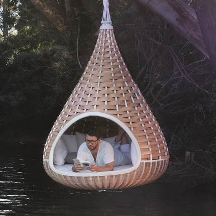 Person lying in a woven hanging pod by a body of water