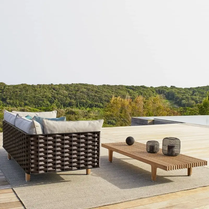 Outdoor patio set with a sofa and coffee table on a deck with a scenic view of trees.