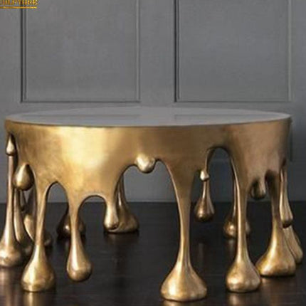 A gold-colored metal coffee table with a cake-shaped design, featuring an abstract pattern of protrusions.