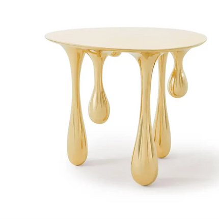 A round, gold metal leg dining table with a modern design. The table has a shiny gold finish, and the leg supports are sculpted in a unique, elegant shape.