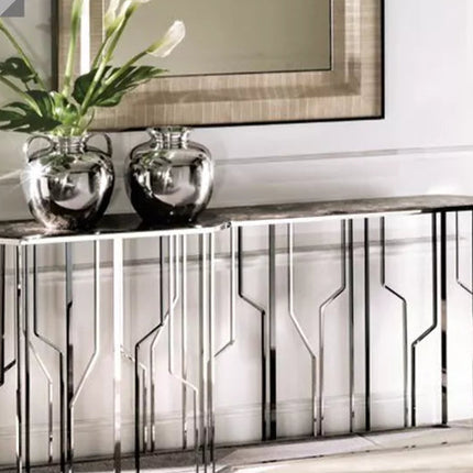 Modern silver console table with a geometric pattern, featuring a marble top and housing for flowers, placed in a bright room setting.