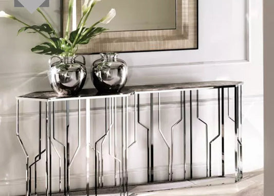Modern silver console table with a geometric pattern, featuring a marble top and housing for flowers, placed in a bright room setting.